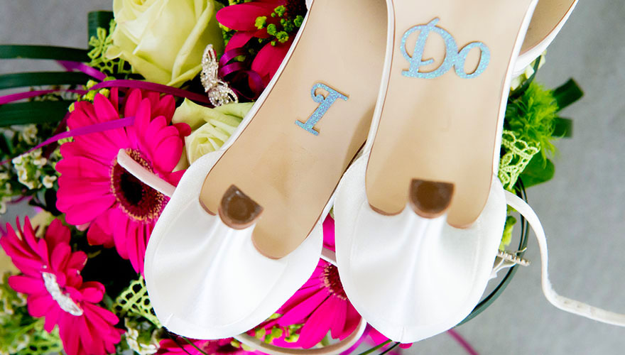 Auf einem Brautstrauss liegen die Brautschuhe verkehrtherum. Auf der Sohle kleben Buchstaben, welche aussagen: I do!