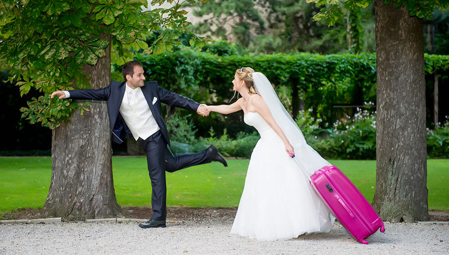 Ein Bräutigam zieht eine Braut hinter sich her, welche wiederum einen Koffer nachzieht.