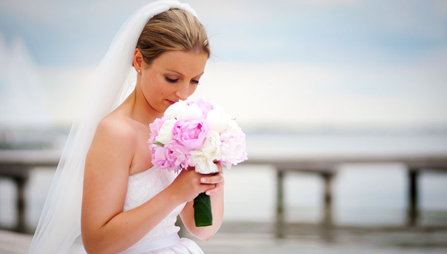 Die Braut sitzt am Strand und geniesst den Duft Ihres Brautstrausses.