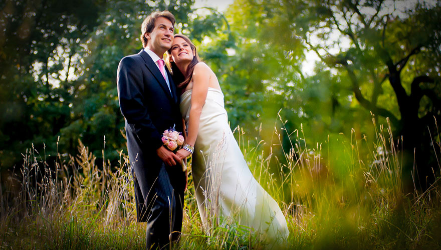 Ein Brautpaar steht auf einer herbstlichen Wiese. Sie halten sich bei den Händen und sehen in den Himmel.