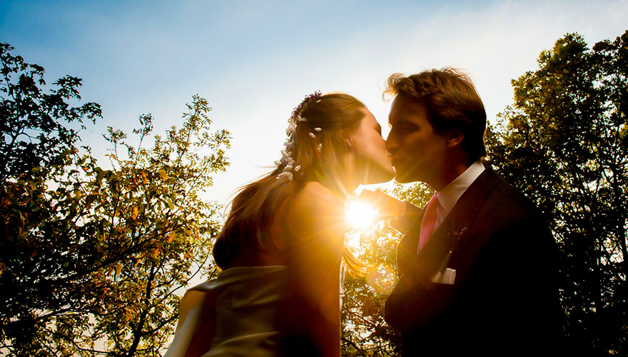 Ein Brautpaar küsst sich am späten Nachmittag. Die Sonne geht gerade unter.