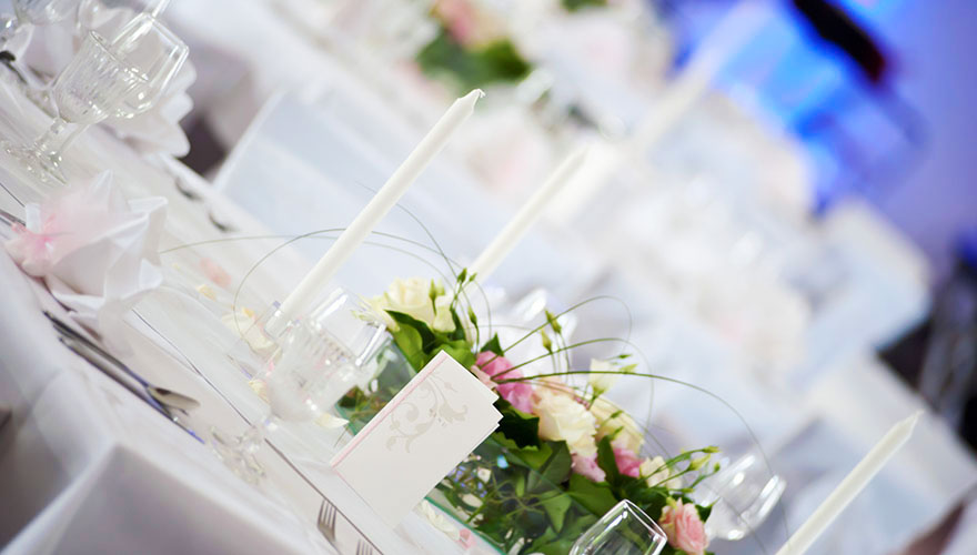 Das Bild einer Hochzeitstafel mit weissen Tischtüchern, Kerzen, Gläsern, Blumen.