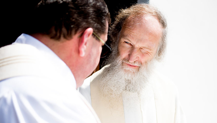 Zwei Priester besprechen etwas. Einer der Priester hat einen langen Bart und die Sonne blendet ihn.