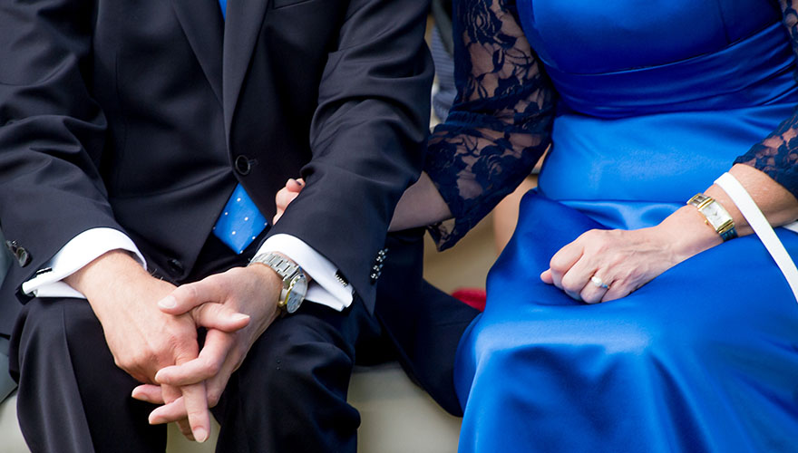 Während einer Hochzeit entdeckt man ein älteres Paar, vielleicht die Brauteltern. Die Dame hält den Arm Ihres Mannes sehr fest. Es wirkt sehr harmonisch. 