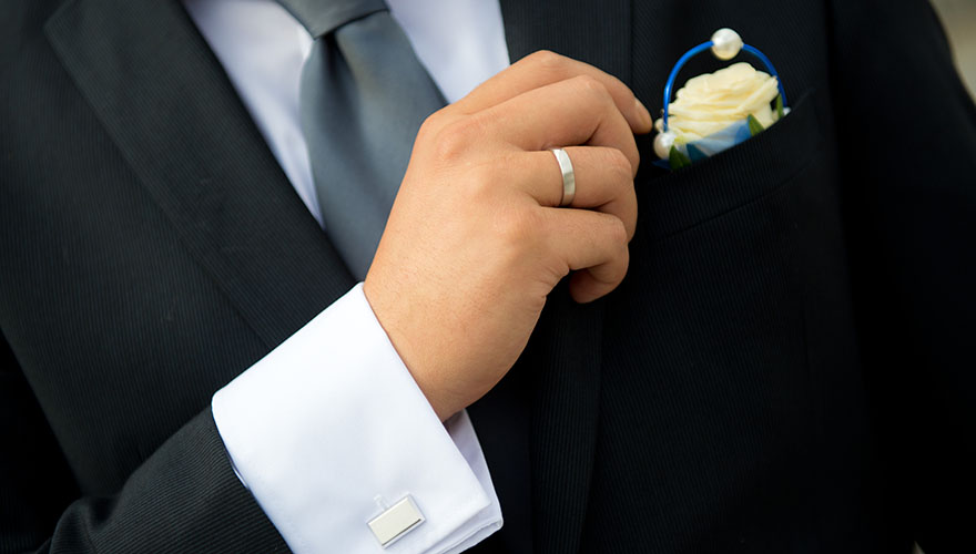 Ein Bräutigam präsentiert stolz seinen Ehering, seine Manschettenknöpfe und seine Ansteckrose am Anzug.