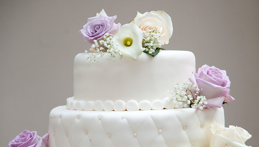 Eine zweistöckige Hochzeitstorte mit echten Rosen und Perlen verziert.