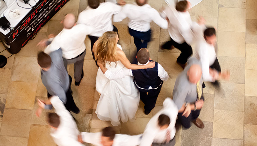 Ein Brautpaar steht und um sie tanzen zehn Männer herum.