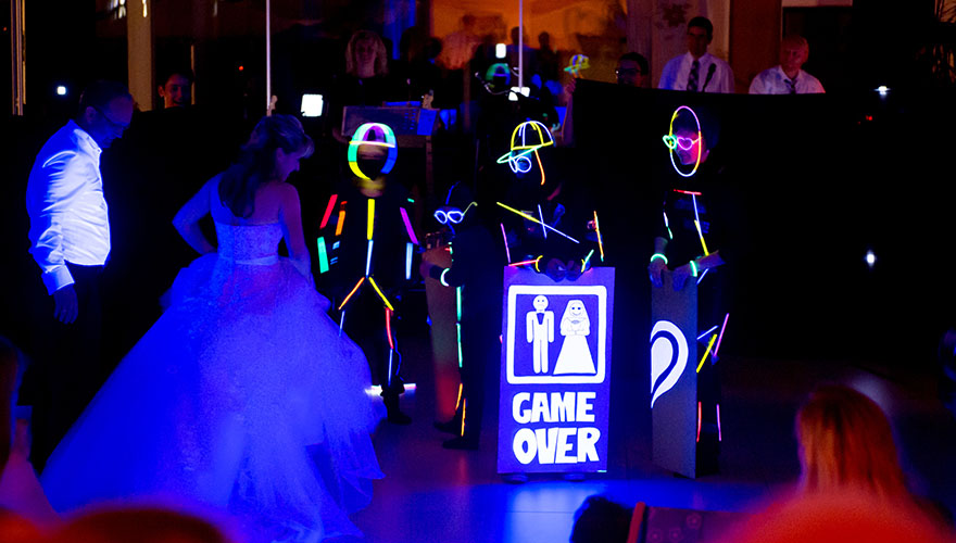 Hochzeitsgäste präsentieren dem Brautpaar eine Lichtshow mit Leuchtstäben. Auf einem Bild steht: Game Over.